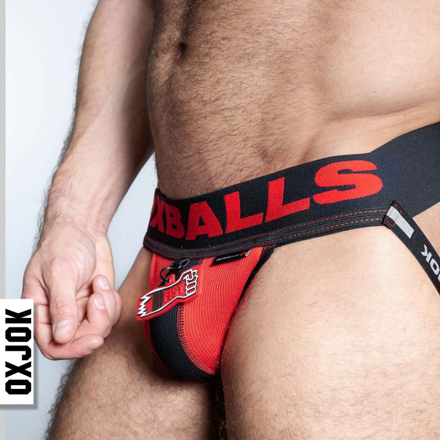 Close-up of man wearing Fisterjock 3d Fist Tagger Jock in black and red with rubber fist tag and Oxjok branding.