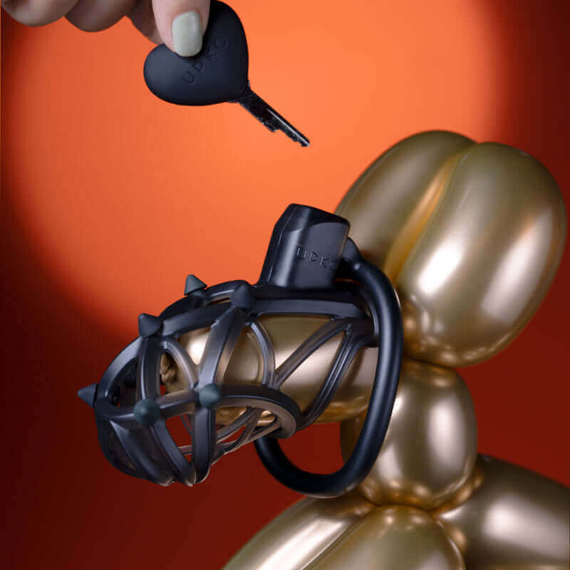 UPKO Caged Beast Male Chastity Device Kit in black, showcasing key and device on a golden balloon figure.