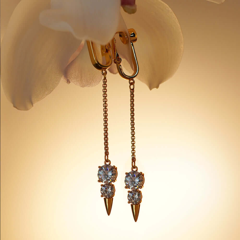 Elegant gold and crystal non-pierced snowman clitoral jewelry hanging against a soft, warm background.