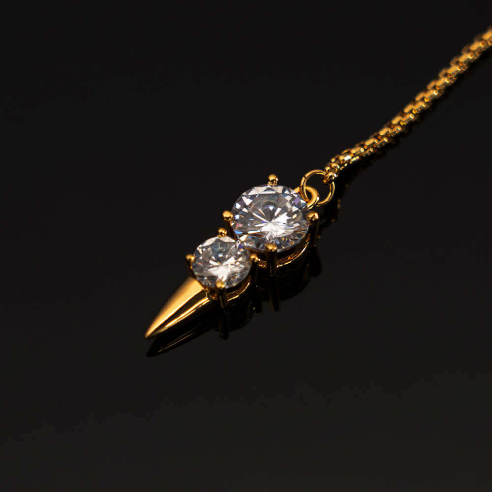 Elegant gold necklace with dual sparkling crystals and a pointed charm on a black background.