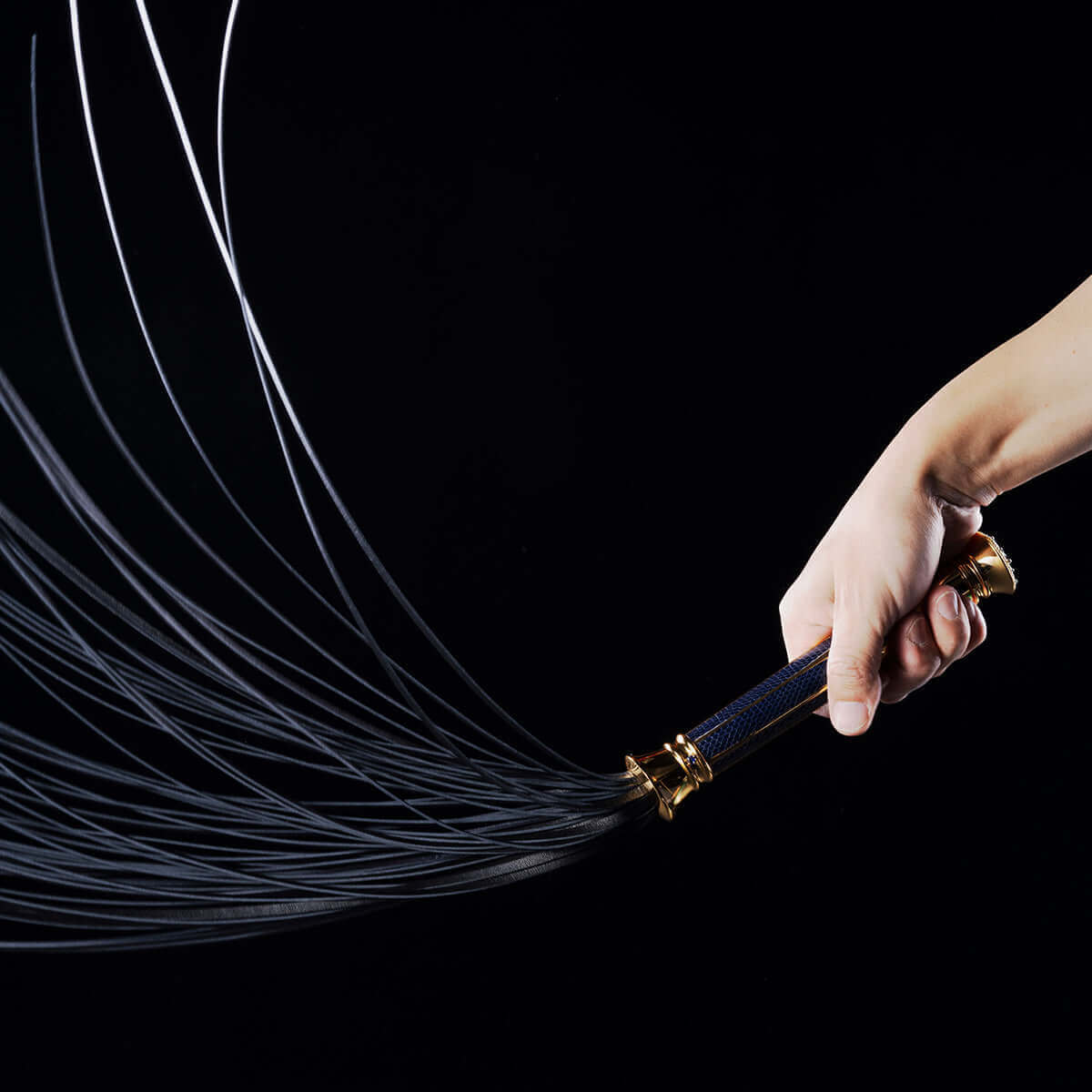 Hand holding the UPKO Black Label Collection Flogger with flowing leather strands against a dark background.