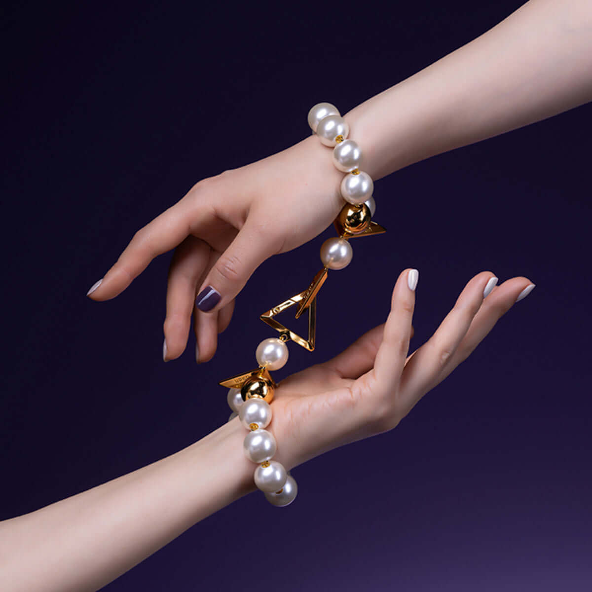 Luxury pearl bracelet handcuffs on wrists, showcasing elegant design with gold accents against a dark background.