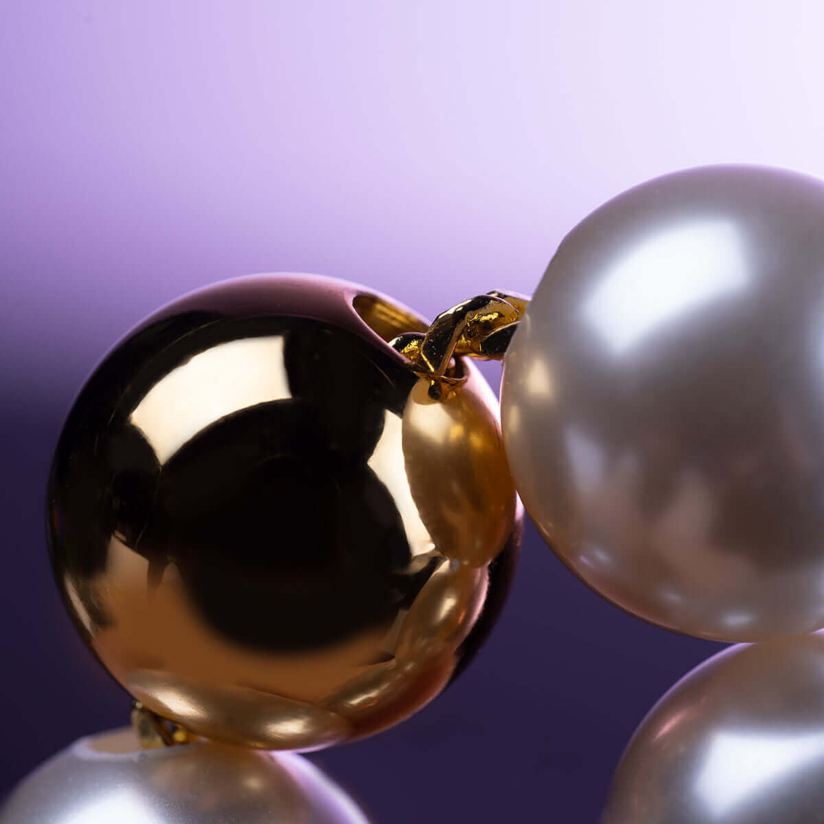 Close-up of UPKO "Moist Eyes" pearl necklace collar featuring gleaming gold and lustrous pearls against a soft purple background.