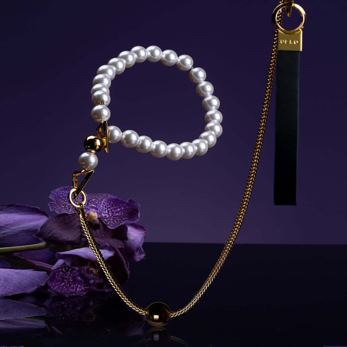 UPKO "Moist Eyes" pearl necklace collar with gold accents, resting on purple flowers, showcasing elegance and brilliance.