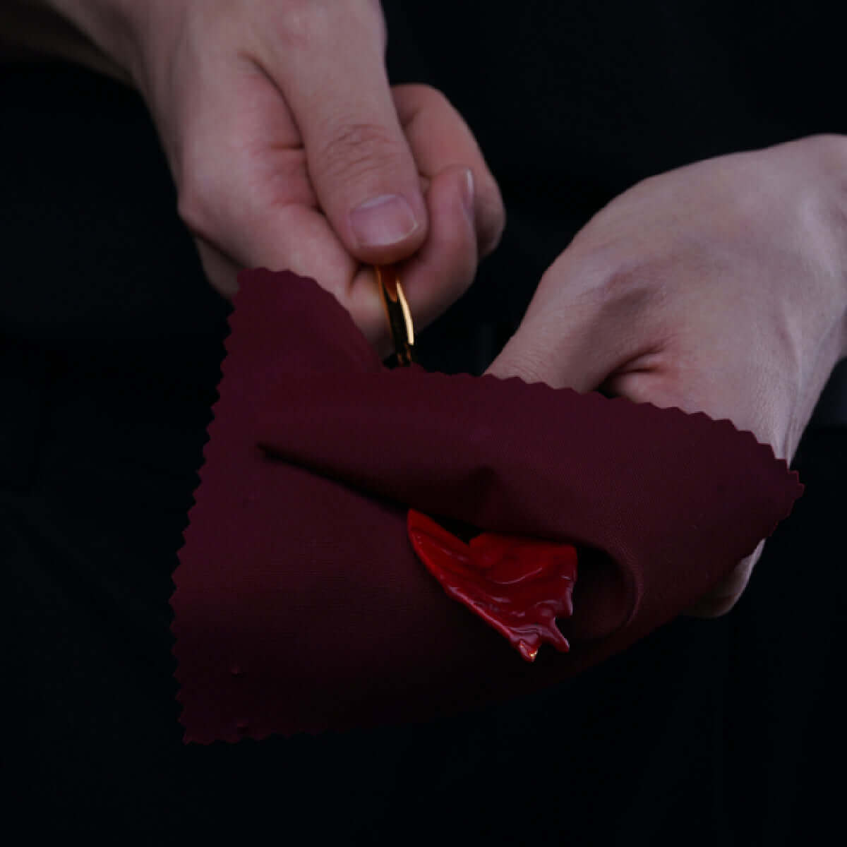 Hands holding a burgundy cloth with red candle wax, demonstrating the UPKO Candle Wax Scraper for wax play.