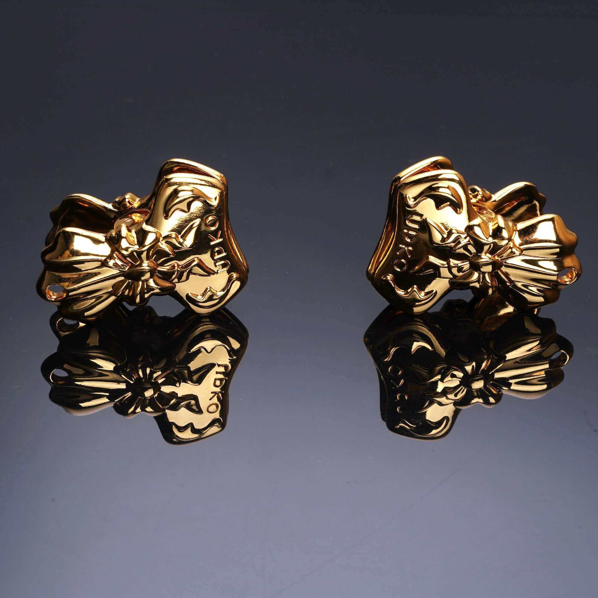 Gold bowknot binder clip style nipple clamps with elegant embossed design, reflecting on a dark surface.