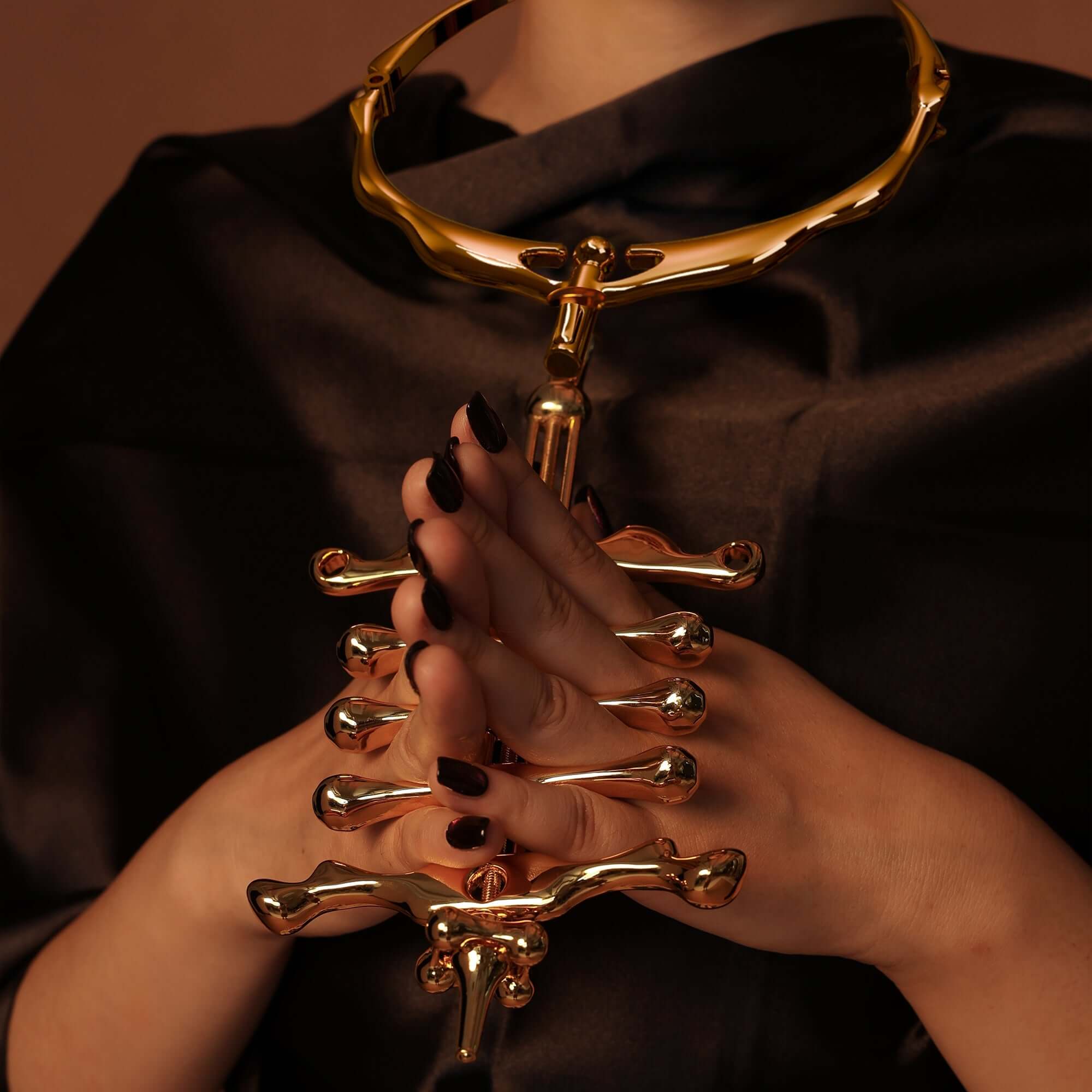 Hands holding a gold UPKO migratory bird collar and finger clamps set against a dark backdrop.