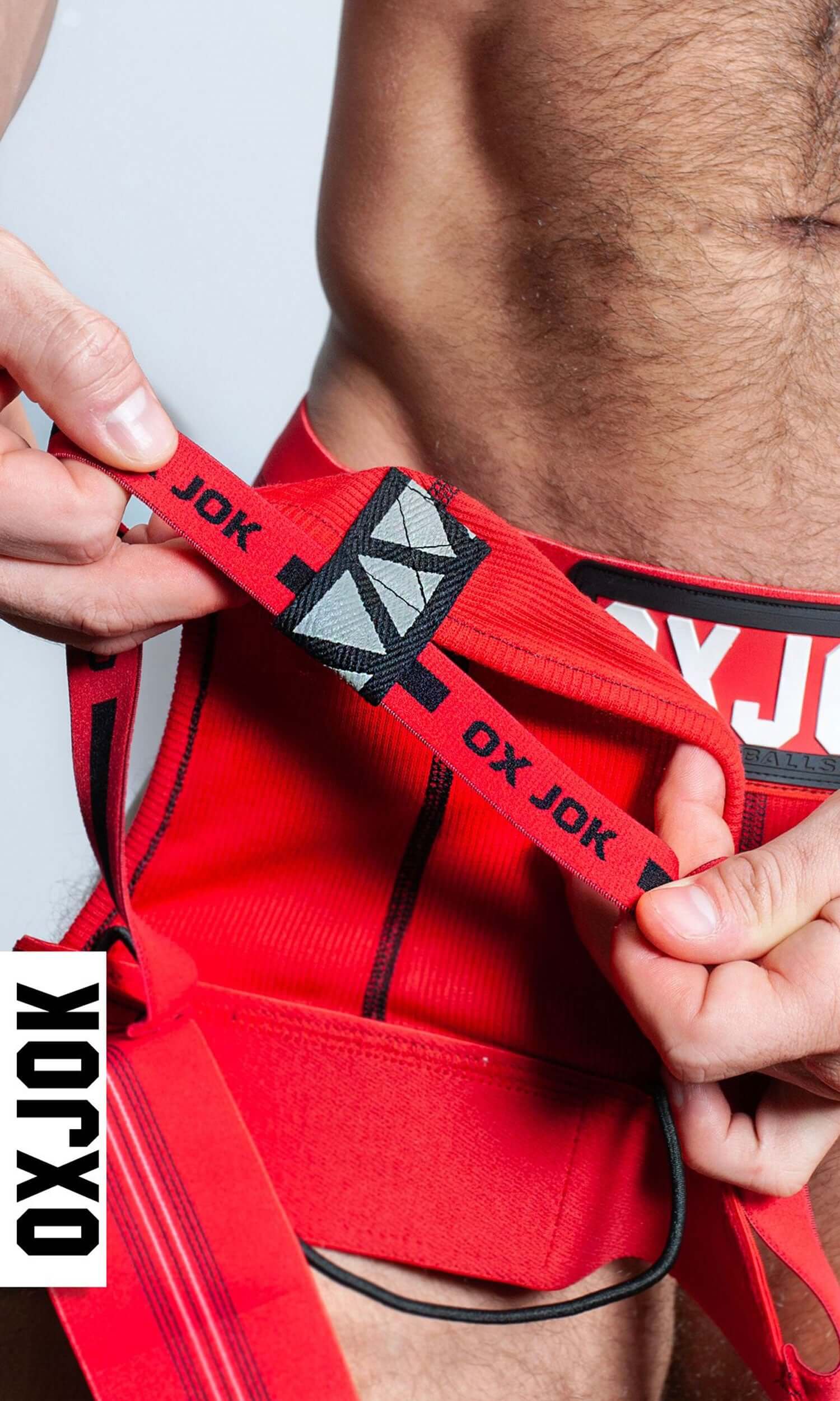 Close-up of person showcasing the red Slingjock Upthrust Slider-Strap Jock with Oxjok branding and adjustable waistband.