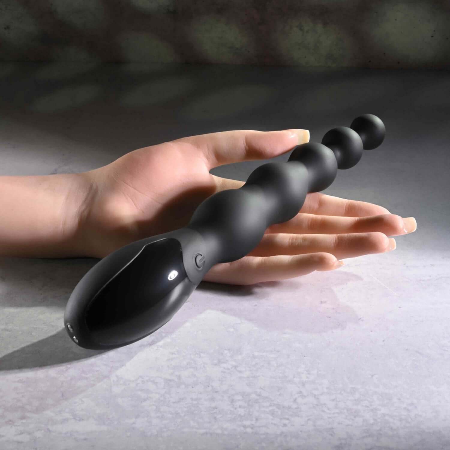 Black flexible beaded anal massager held in hand, featuring graduated bulbs for enhanced pleasure and nine vibrating patterns.