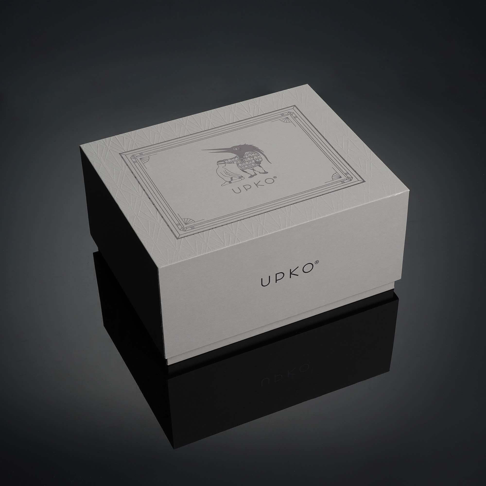 Elegant UPKO packaging box on a dark reflective surface, showcasing luxury branding and design elements.