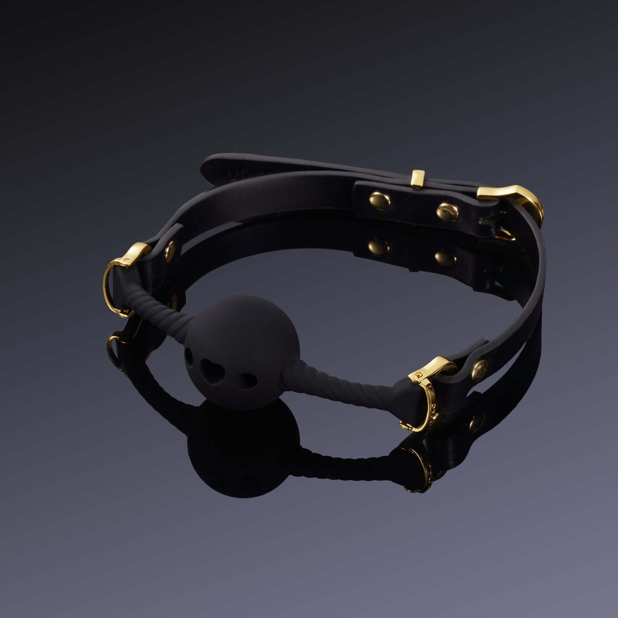 Black heart-shaped breathable mouth gag with gold hardware and high-quality silicone on a reflective surface.