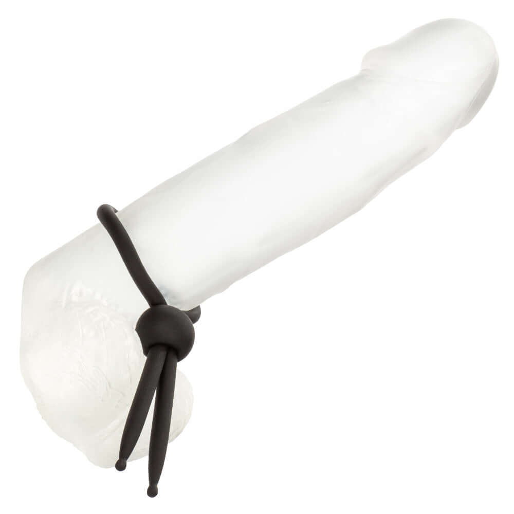 Adjustable black Alpha Liquid Silicone Lasso enhancer cinched on a clear cylindrical object for intimate control and enhancement.