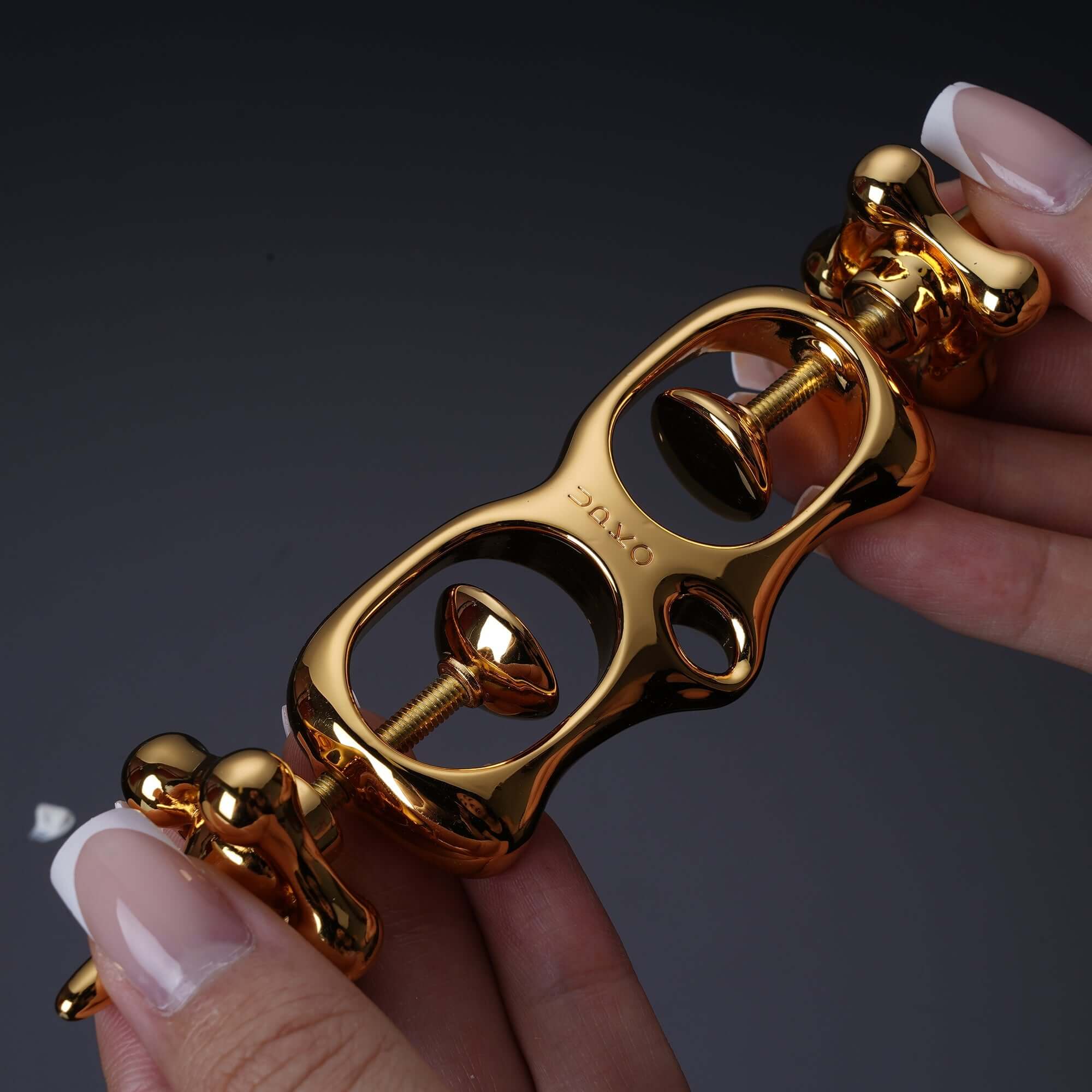 Golden UPKO Thumb Metal Cuffs held in hands, showcasing the unique design and pull-string mechanism for restraint.