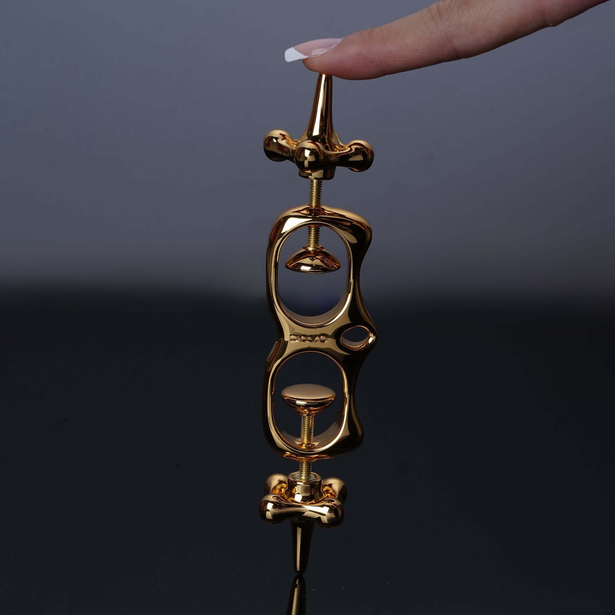 Thumb Metal Cuffs in gold, showcasing a unique design, held by a finger against a dark background.