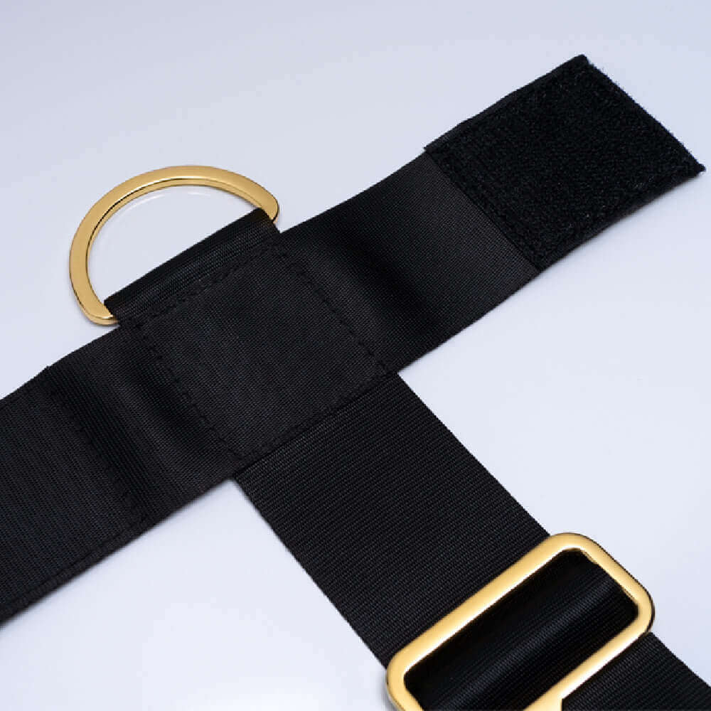 Close-up of UPKO adjustable bed restraint strap showing black fabric, gold hardware, and Velcro for secure attachment.