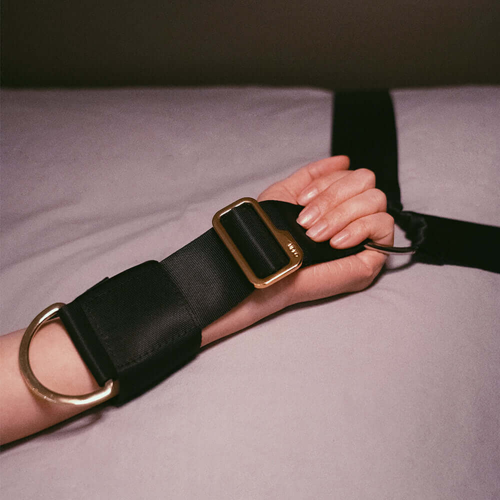 Adjustable bed restraint strap in black and gold on a hand, showcasing comfort and style for BDSM experiences.