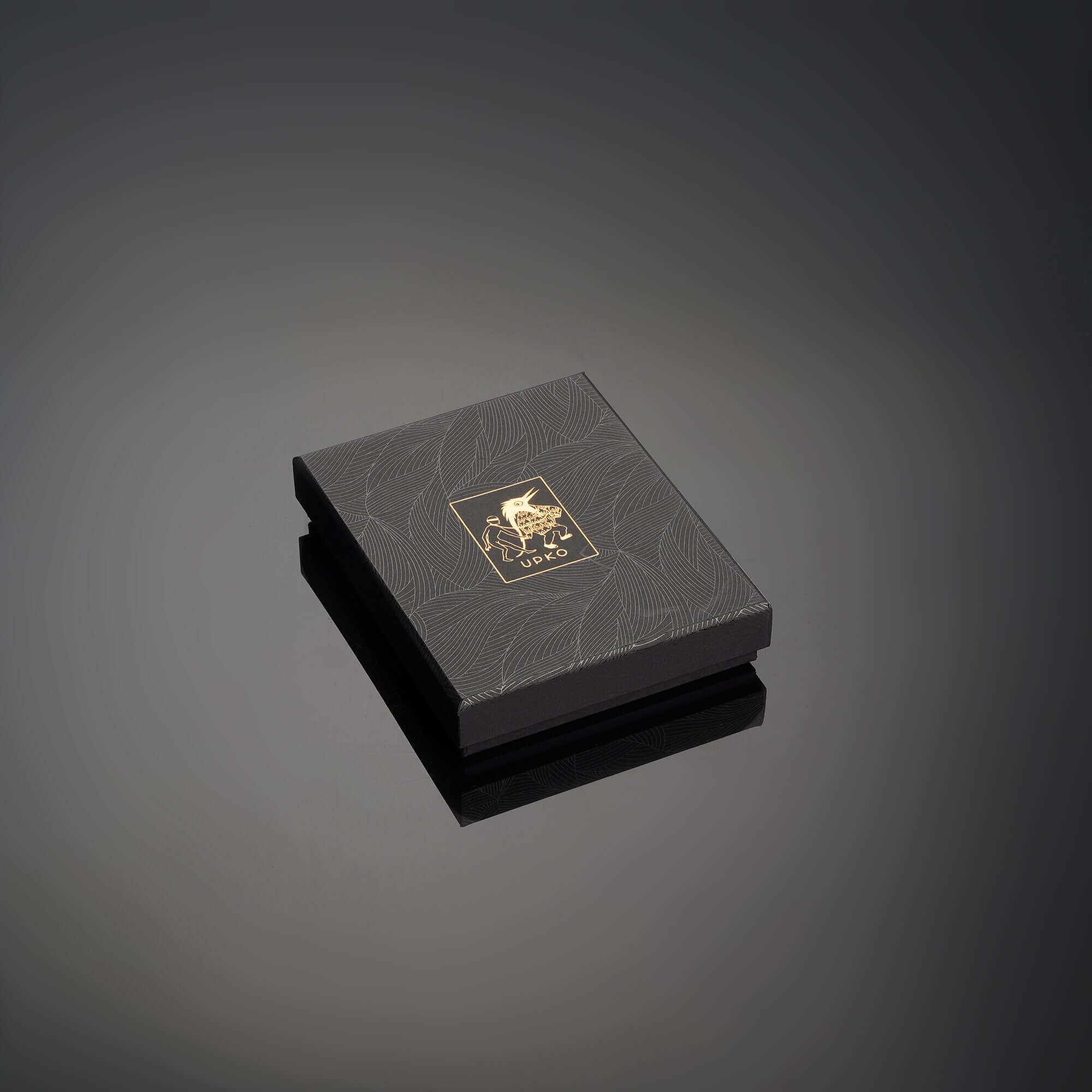 Elegant black packaging box with gold logo design, reflecting a luxurious product inside, set against a dark background.