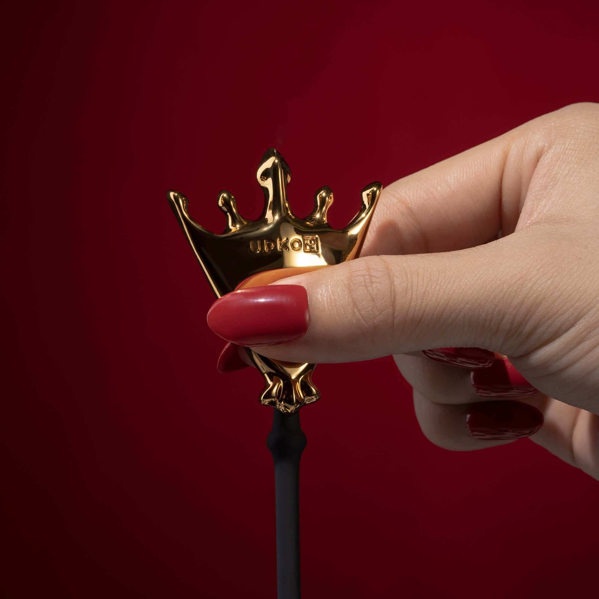 Hand holding a gold crown-shaped handle of the Queen Premium Metal Pleasure Balls from The Chess Collection.