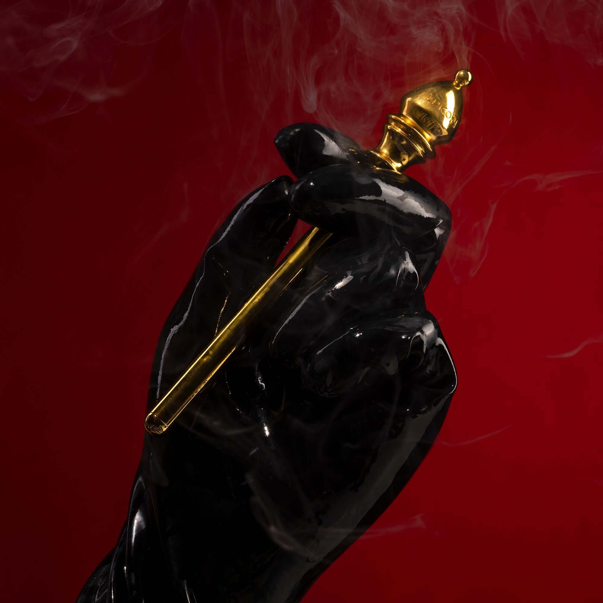 Black hand holding a gold bishop piece against a red background, with smoke for an artistic touch.