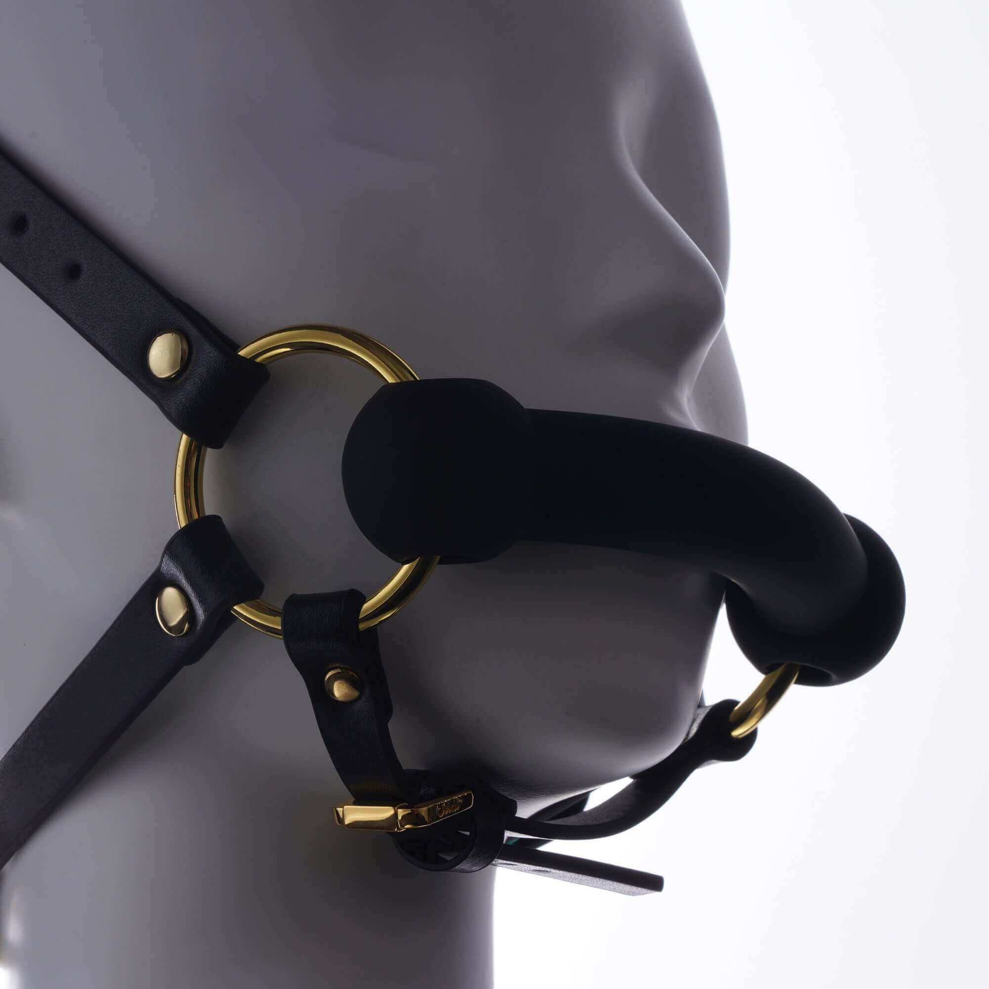 Adjustable leather mouth gag harness with gold accents on a mannequin head, designed for restraint and control.