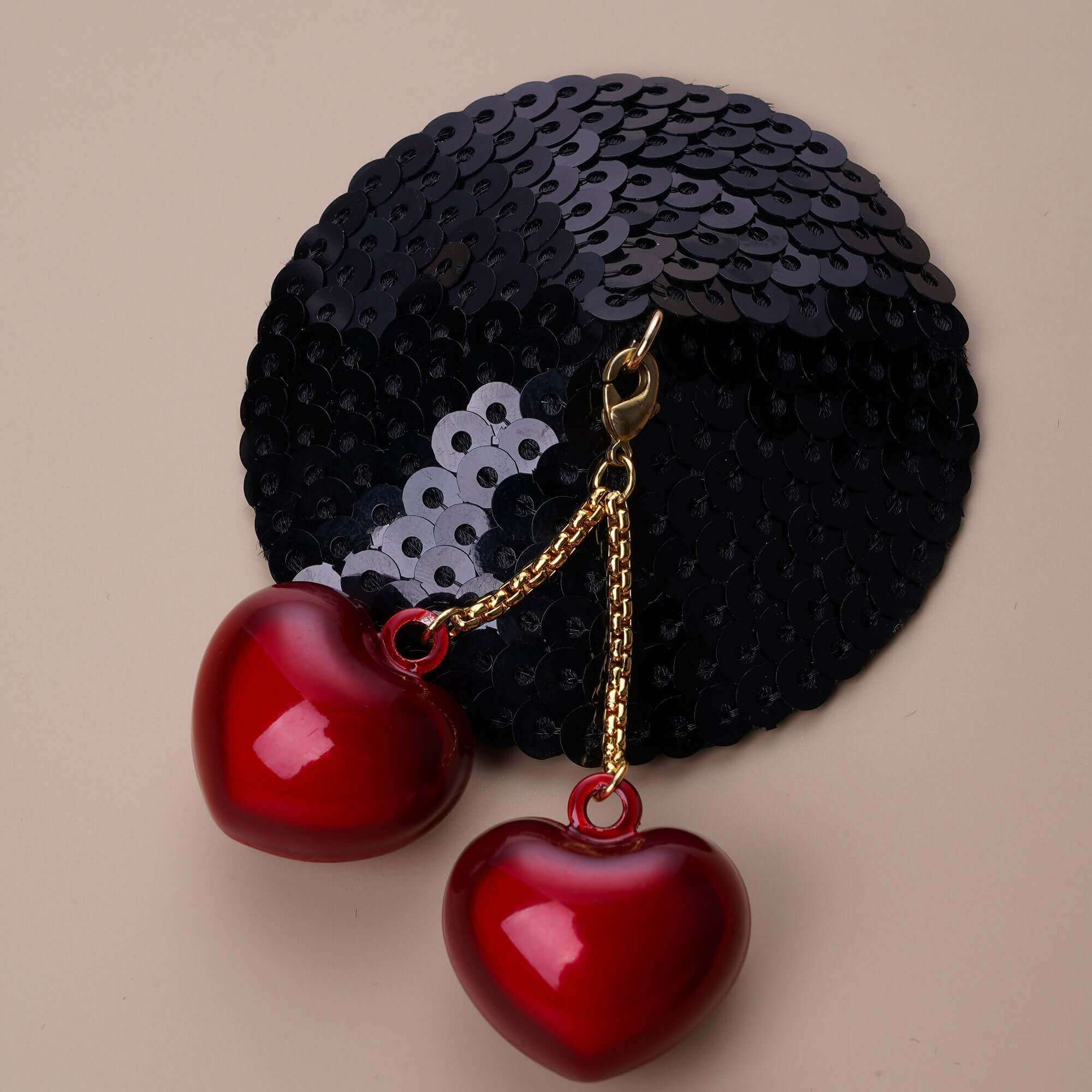 Black sequin nipple pasty with red heart-shaped bells on detachable chains for stylish, reusable adornment.