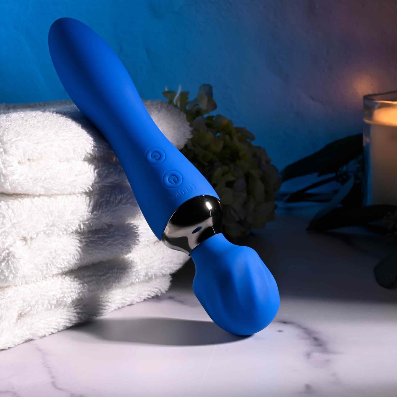 Stylish blue wand massager with dual motors, textured head, on a towel with soft lighting, showcasing its sleek design.