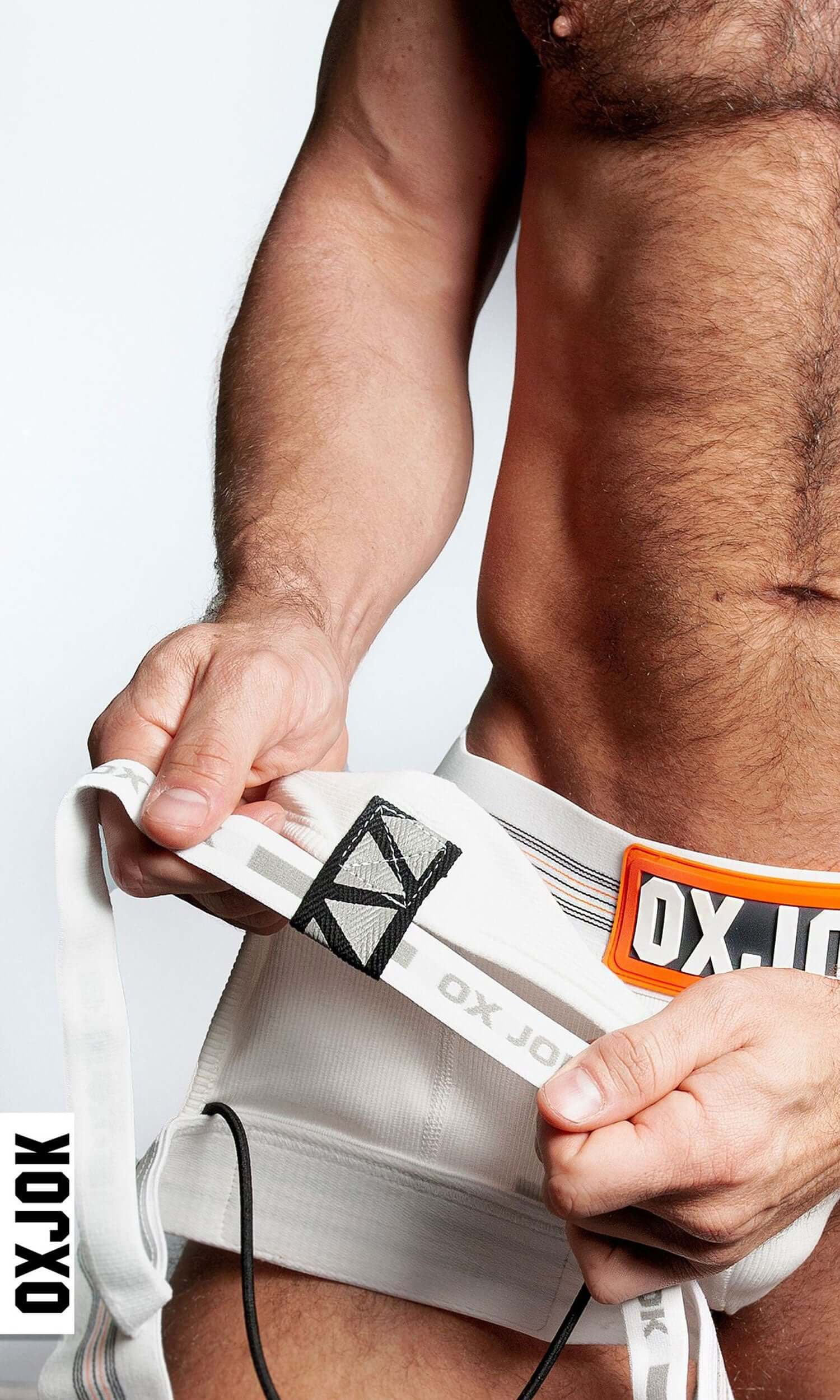 Man wearing white Oxjok Slingjock Upthrust Slider-Strap Jock adjusting waistband for a perfect fit.