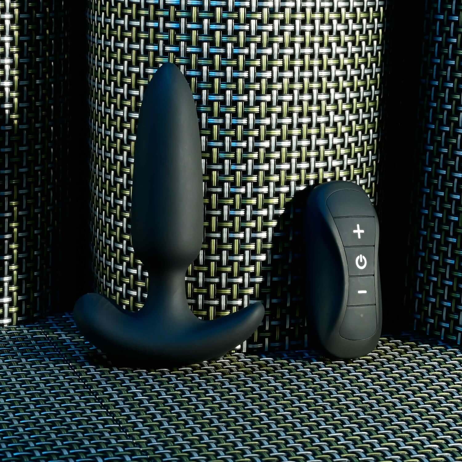 Black Beauty remote control anal plug with tapered tip and safety base next to the remote controller on textured surface.