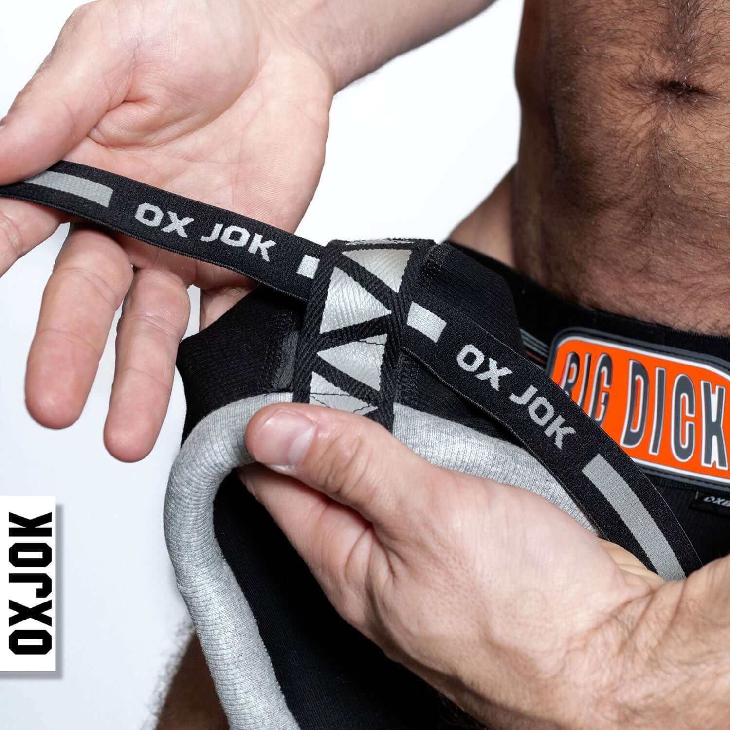 Man holding Bulger the Big Pouch Jock Black Iron with padded strap detail and "OX JOK" branding.