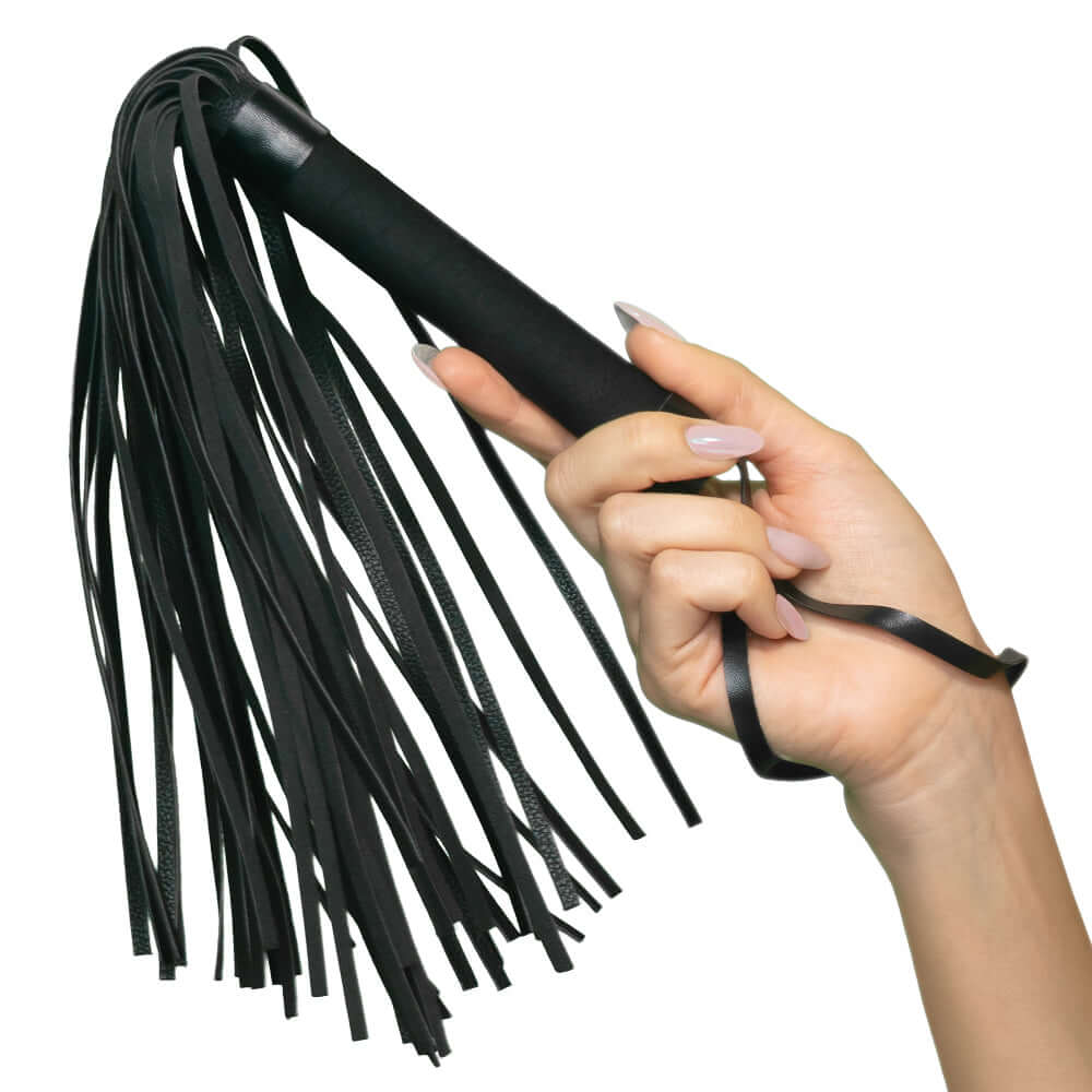 Hand holding black Nocturnal Collection Flogger with soft teasing tassels designed for sensory play.